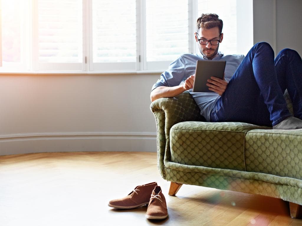 En mand sidder på en sofa og fokuserer på at bruge en tablet i en hyggelig stue